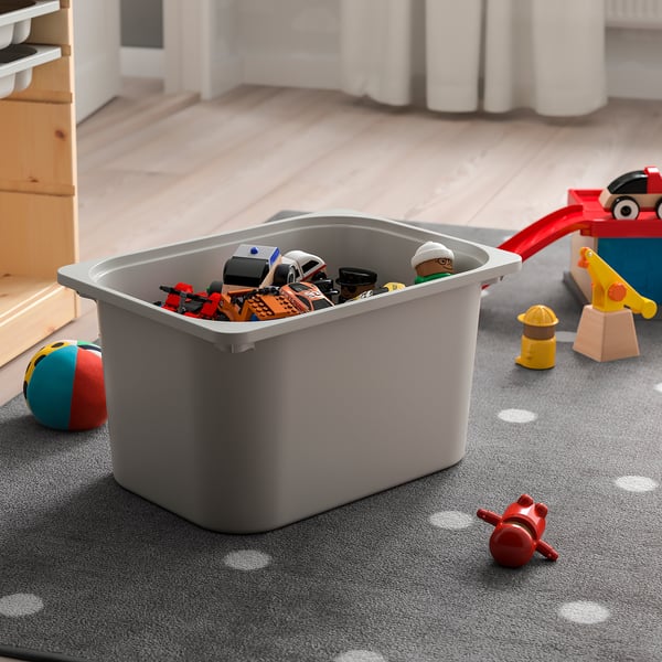 Gray TROFAST bin filled with colorful toys on a gray carpet, storing and organizing childrens playthings neatly.