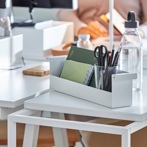 White TROTTEN trolley holds office supplies: notebooks, pens, scissors, and a water bottle. Fits near desks, easy to move with casters.