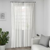 White sheer curtain by window with greenery, chair, and art. Leaf pattern for light and privacy.