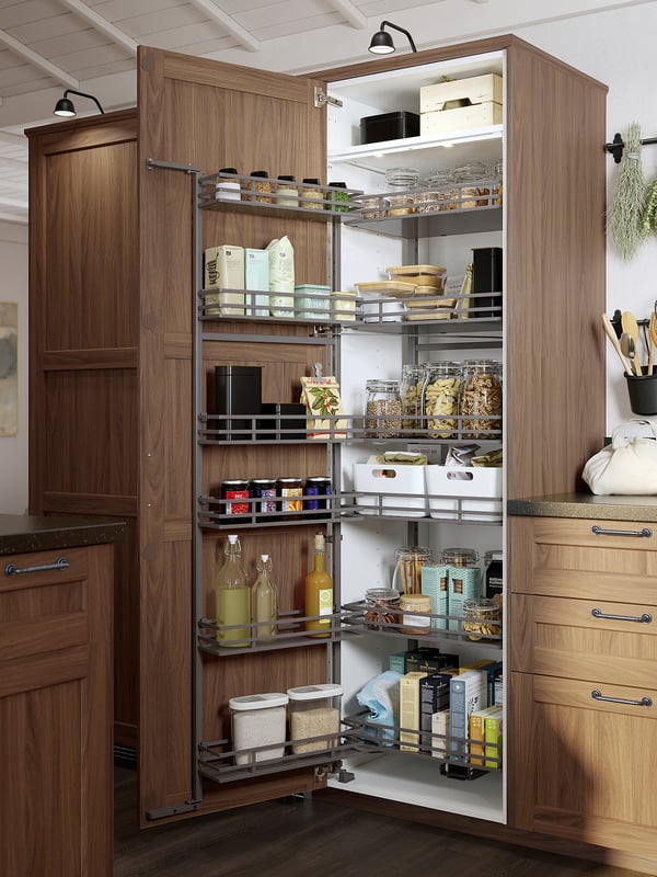 Well-organized wooden kitchen cabinet with pull-out shelves, storing jars, bottles, and containers, illuminated by a stylish lamp.