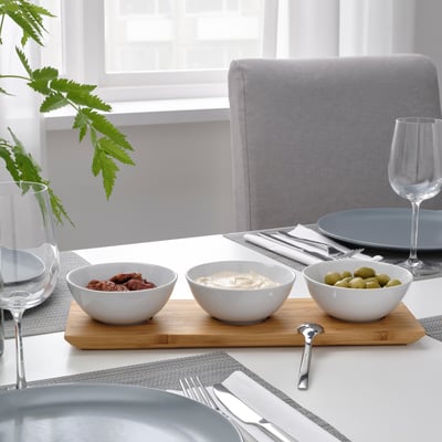 A dining table set with TYNGDLÖS serving tray and three bowls filled with snacks, utensils, and wine glasses.