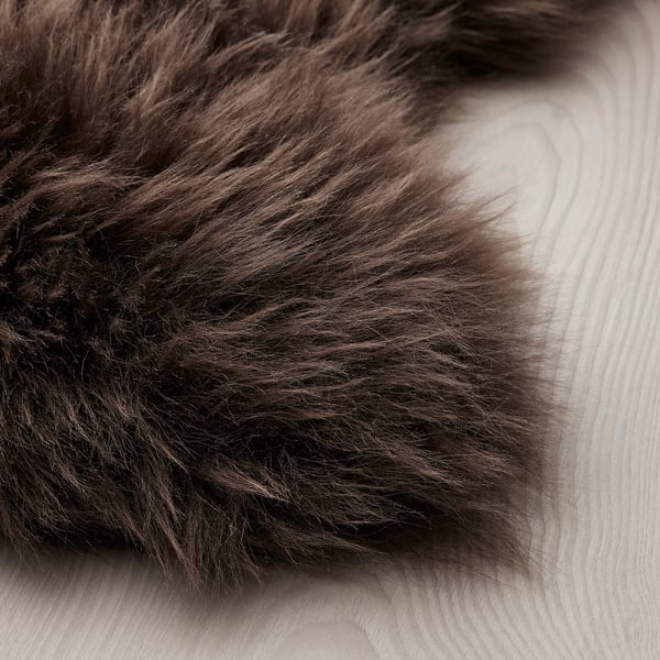 Close-up of soft, luxurious brown sheepskin rug on light wooden floor, showing its fluffy texture and natural beauty.