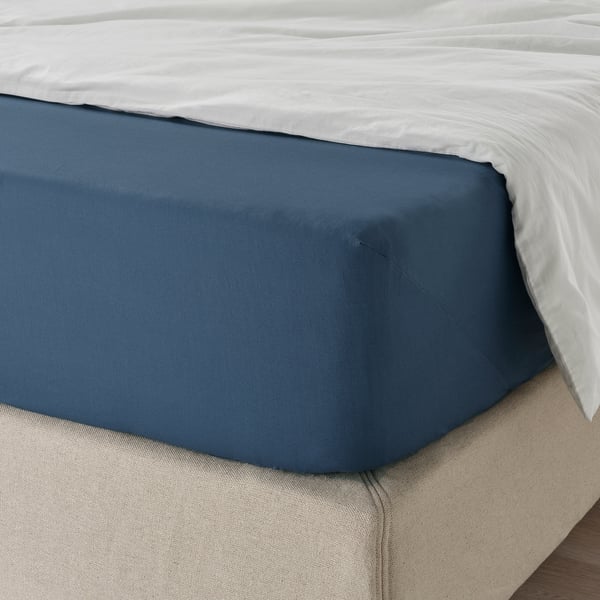 Neatly made bed with dark blue sheet, elastic edges, smooth texture.
