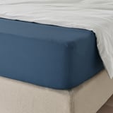 Neatly made bed with dark blue sheet, elastic edges, smooth texture.