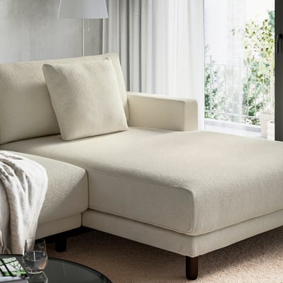 Beige sectional sofa with chaise, pillows, and blanket, placed near a window.