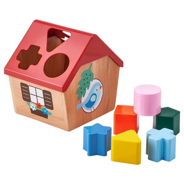 A red UPPSTÅ shape sorter toy resembling a birdhouse with shapes around. Its for learning shape and color recognition.