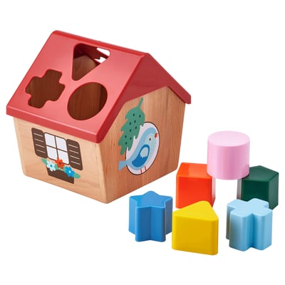 A red UPPSTÅ shape sorter toy resembling a birdhouse with shapes around. Its for learning shape and color recognition.