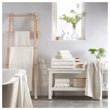 Modern bathroom with white VÅGSJÖN towels, a wooden towel rack, and a window with potted plants.