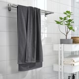 Gray VÅGSJÖN towel on bar in tiled bathroom, with shelf holding plant and towels.