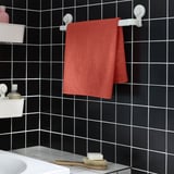 VÅGSJÖN red towel hangs between white hooks on dark tiled wall. Small, rectangular, adjacent to sink with toiletries.