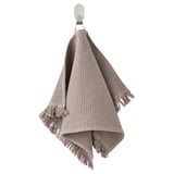 A light grayish-brown VALLASÅN towel hanging, made of cotton and viscose, featuring a waffle texture and fringe edges.