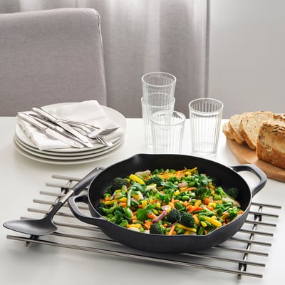 Cast iron skillet with stir-fried vegetables on a trivet, plates, napkins, and cups nearby.