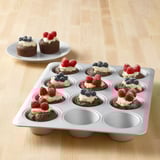 Muffin tin filled with brownie bites topped with fruit and frosting.