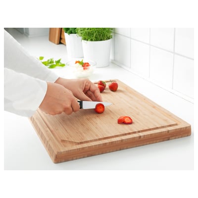Person slices strawberries with small knife on wooden cutting board.