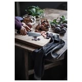 Person slicing beets on a wooden table with a silver VARDAGEN knife, surrounded by vegetables, with a gray cloth nearby.