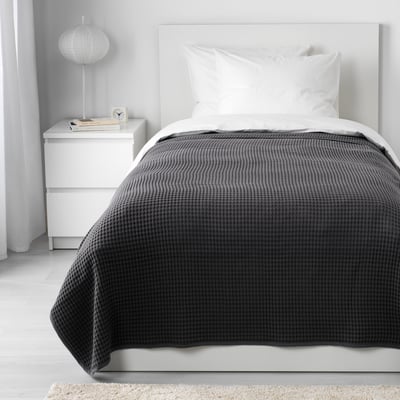 VÅRELD gray cotton bedspread covers a white single bed, larger than bedside drawers.