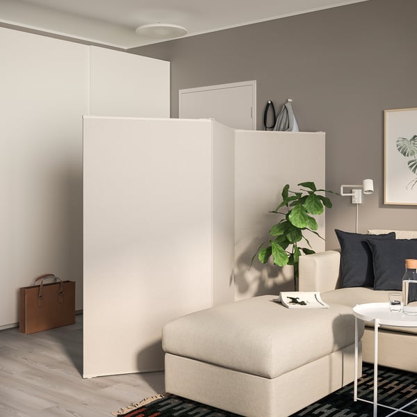 Beige room divider in living room, separating sleeping area with bed & plant area.