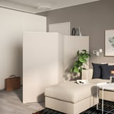 Beige room divider in living room, separating sleeping area with bed & plant area.