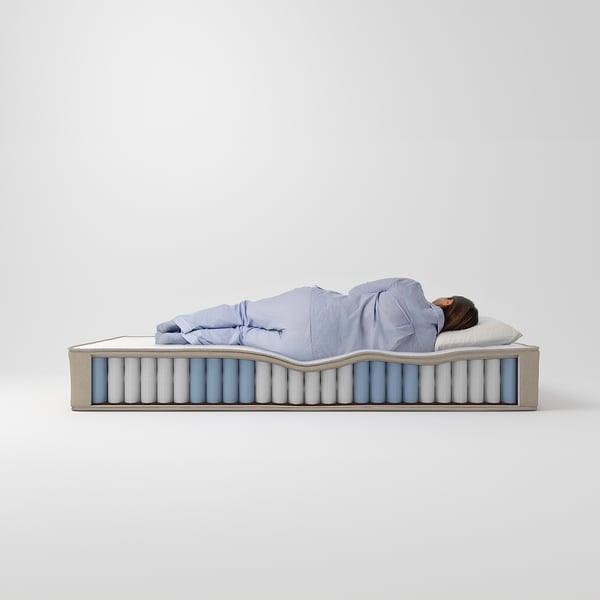 A person sleeps on a blue-covered, extra-firm mattress with pocket springs, displayed against a white background.
