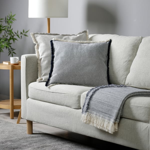 Modern living room with grey sofa, blue/white cushions, throw, lamp, side table, mug, plant.
