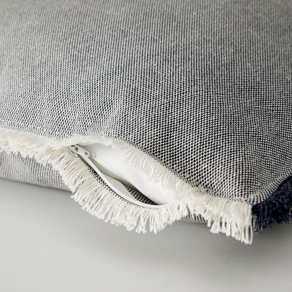 Image shows a close-up of a grey cushion cover with a zipper and fringed edges, highlighting its detailed texture and craftsmanship.