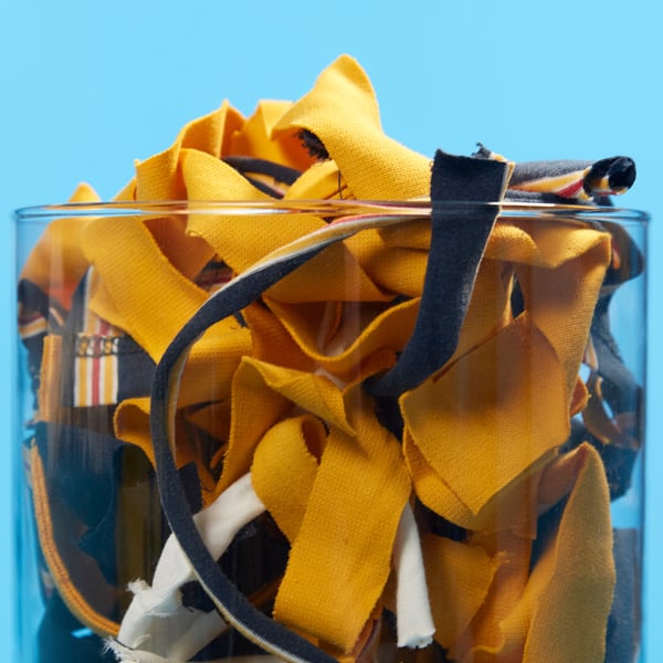 VÄXELBRUK yellow cushion cover, round, with black zipper, in clear container. The cover is larger than the container.