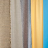 Four fabric swatches in shades of gray, brown, and beige hung vertically, showcasing textured weaves and color variations.