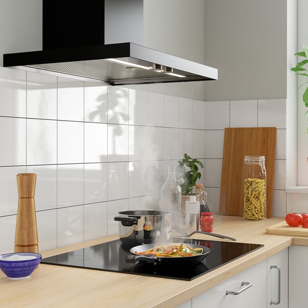 Modern kitchen with induction stove, colorful veggies, wooden counter & gray backsplash.