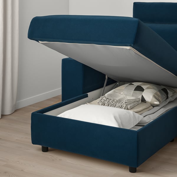 Blue sofa with lift-up storage compartment, showing neatly folded white blanket inside.