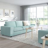 Modern living room with light blue VIMLE sofa, light wood coffee table, grey rug, & large windows.