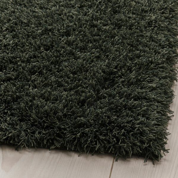 Dark green, soft, thick rug folded on wooden floor.