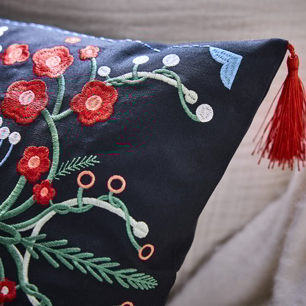 Black cushion with intricate embroidered flowers, green stems, and red tassel. Detailed, high-quality craftsmanship.