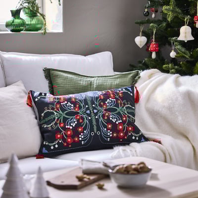 Christmas-themed living room with VINTERFINT black embroidered pillow on white sofa, beside decorated christmas tree.