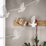 White paper dove garland over brown wood, smaller than surrounding greenery.