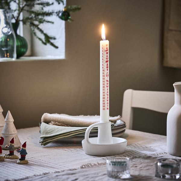 Christmas scene with VINTERFINT white candle, lit, on table with gnomes, napkins, and glasses.
