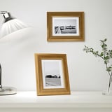 Two gold frames: one on wall, one on table, with bw photos, lamp, vase.