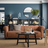 Modern living room with VISKAFORS brown leather sofa, black coffee table, dark blue walls, round mirror, and decorative shelves.