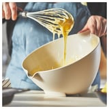 A person whisking batter in a white VISPNING bowl with a spout, wearing a blue apron.