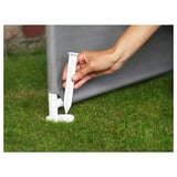 Hand placing white plastic stake into grassy area against gray mesh structure.