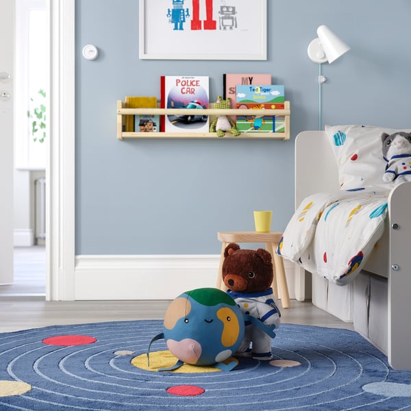Habitación para niños con cama para niños pequeños, alfombra azul, peluche de astronauta y libros.