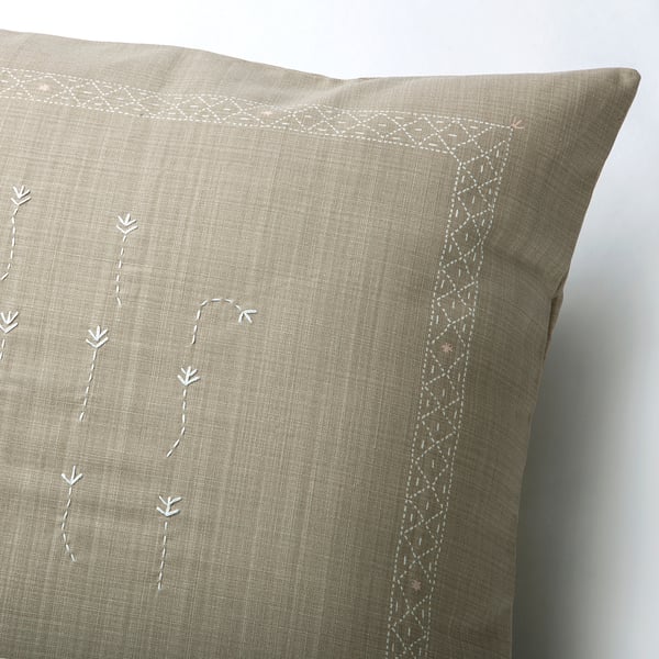 Elegante cojín beige con sutiles diseños florales bordados a mano y bordes intrincados.
