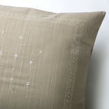 Elegante cojín beige con sutiles diseños florales bordados a mano y bordes intrincados.