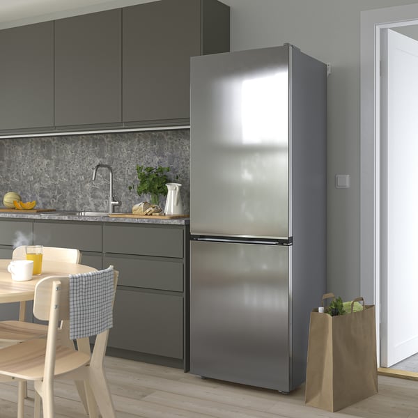 Cocina moderna con nevera de acero inoxidable, armarios oscuros, mesa de comedor y placa para salpicaduras de mármol. Bolsa de supermercado cerca.