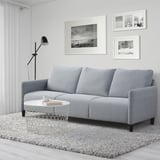 Sofá gris de 3 plazas, lámpara, alfombra, mesa de centro en amplia habitación.