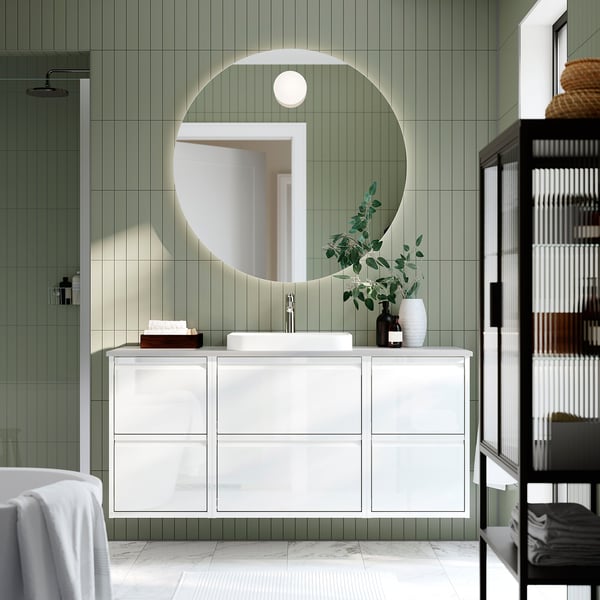 Tocador blanco de pared con espejo, lavabo, grifo moderno, cajones, azulejos verdes, estantes negros con toallas.