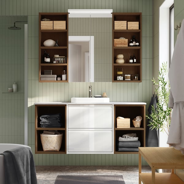 Tocador de baño ÄNGSJÖN blanco con almacenamiento abierto/cerrado, lavabo, artículos de tocador, armario con espejo, banco de madera, planta, azulejos verdes.