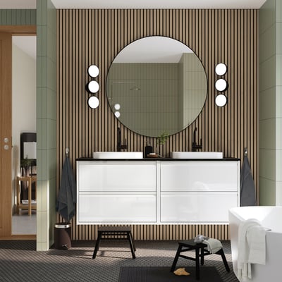 Baño moderno con tocador blanco ÄNGSJÖN, espejo redondo, detalles negros, dos lavabos y toallas.