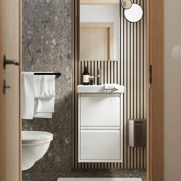 Moderno mueble de baño blanco ÄNGSJÖN con cajones y lavabo, junto a pared de mármol con toallero.
