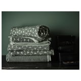 Tres pilas de toallas estampadas gris/verde sobre madera oscura.