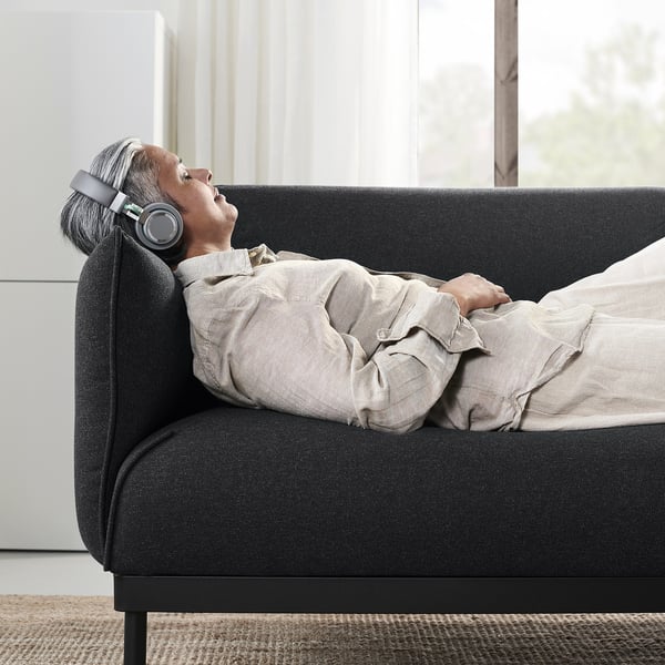 Una persona se relaja en un sofá gris con auriculares. El sofá es elegante y moderno, con un diseño cómodo y a medida.